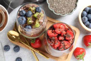 Lezzetli çikolatalı pudingler, chia tohumları ve bardaklar içinde gri masada, düz yerde.