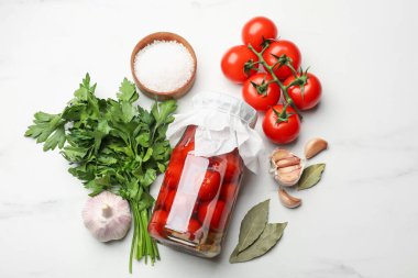 Kavanozda domates turşusu ve beyaz mermer masada malzemeler.