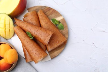 Lezzetli meyve dürümleri, nane, mango ve kayısılar beyaz masada, düz yerde. Metin için boşluk