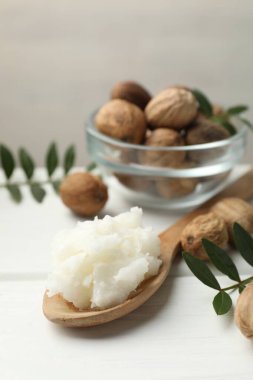 Doğal Shea yağı, fındık ve yapraklar beyaz ahşap masada, yakın plan.