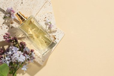 Bir şişe parfüm ve soluk sarı arka planda güzel leylak çiçekleri. Metin için boşluk