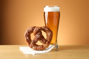 Lezzetli kraker ve bir bardak bira ahşap masada bej renkli arka planda, yakın plan.