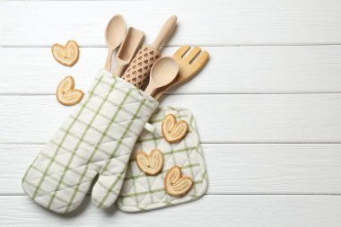 Farklı mutfak aletleri fırın eldiveni ve beyaz ahşap masa üzerinde avuç içi kurabiyeler, düz yatak. Metin için boşluk