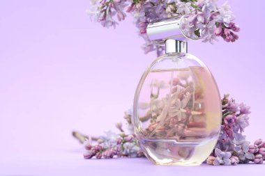 Parfüm şişesi ve mor arkaplanda leylak çiçekleri, yakın plan. Metin için boşluk