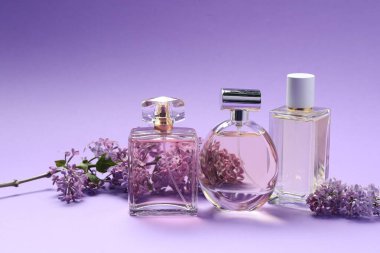 Mor arkaplanda leylak çiçekli parfüm şişeleri ve dallar, yakın plan.