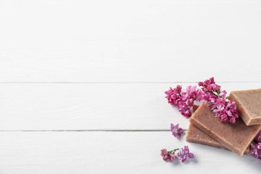 Beyaz ahşap masada sabun çubukları ve leylak çiçekleri. Metin için boşluk