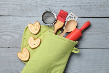 Farklı mutfak aletleri fırın eldiveni ve açık gri ahşap masa üzerinde avuç içi kurabiyeler.