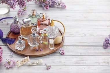 Beyaz ahşap masada parfüm şişeleri, aksesuarlar ve leylak çiçekleri. Metin için boşluk