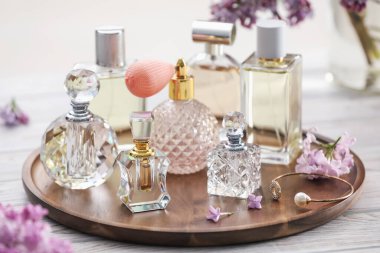 Beyaz ahşap masada, parfüm şişeleri ve leylak çiçekleri, yakın plan.