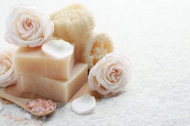 Sabun çubukları, deniz tuzu, lif süngeri ve beyaz desenli masa üzerindeki çiçekler, yakın plan. Metin için boşluk