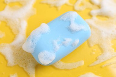 Sarı arka planda köpük olan sabun çubuğu, üst görünümde.