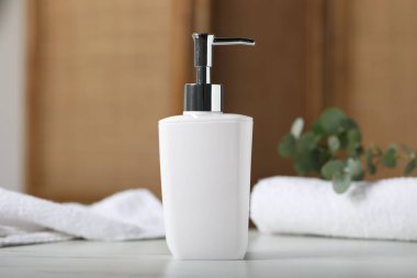 Şişedeki sıvı sabun, havlular ve okaliptüs dalı kapalı alandaki beyaz mermer masa üzerinde.