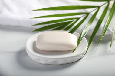 Sabun çubuğu, havlu ve palmiye yaprağı beyaz mermer masada, yakın plan.