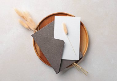 Boş davetiye kartı, zarf, tahta tepsi ve bej arka planda kuru çiviler.