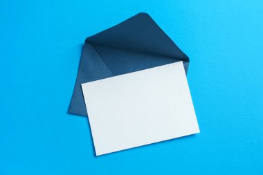 Açık mavi arka planda boş davetiye ve zarf, üst manzara. Tasarım için boşluk