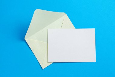 Açık mavi arka planda boş davetiye ve zarf, üst manzara. Tasarım için boşluk