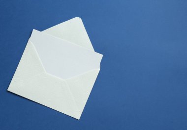 Mavi arka planda boş davetiye ve zarf, üst manzara. Metin için boşluk