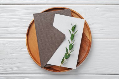 Boş davetiye kartı, zarf, tepsi ve dal beyaz ahşap masa, üst görünüm