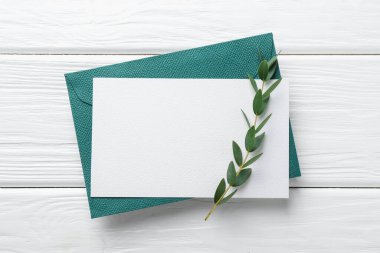 Boş davetiye kartı, zarf ve dal beyaz ahşap masa, üst manzara. Tasarım için boşluk