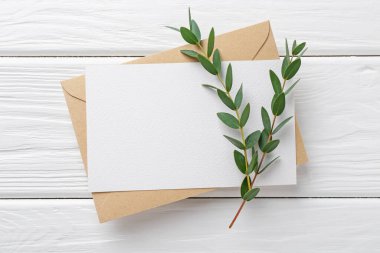 Boş davetiye kartı, zarf ve dallar beyaz ahşap masa, düz yatıyordu