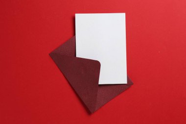 Kırmızı arka planda boş davetiye ve zarf, üst manzara. Tasarım için boşluk