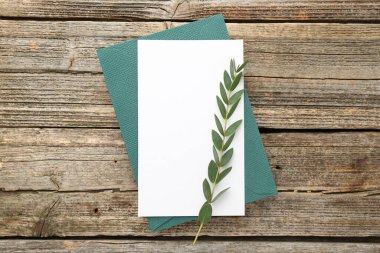 Boş davetiye kartı, zarf ve yeşil dal, ahşap masa, üst manzara.