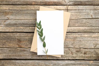 Boş davetiye kartı, zarf ve yeşil dal, ahşap masa, üst manzara.