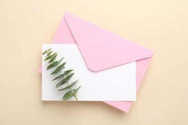 Bej arka planda boş davet kartı, zarf ve okaliptüs dalı, üst görünüm
