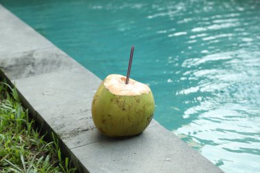 Yeşil hindistan cevizi, ferahlatıcı bir içecek ve açık havuzun yanında saman.