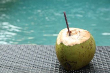 Yeşil hindistan cevizi, ferahlatıcı bir içecek ve hasır saman ile açık havuz kenarında yüzme masasının yanında, yakın plan. Metin için boşluk