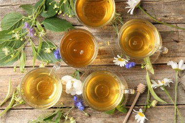Cam bardaklarda Aromatik bitki çayı, çiçekler ve yeşil yapraklar ahşap masada, düz uzanmış