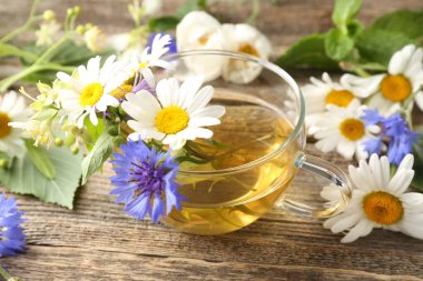 Cam bardakta Aromatik bitki çayı ve ahşap masada çiçekler, yakın plan.