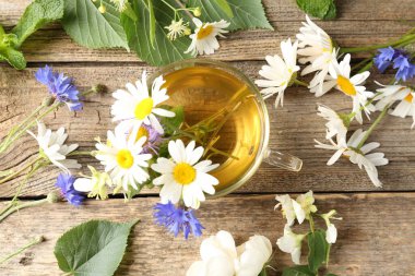 Cam bardakta Aromatik bitki çayı, tahta masada çiçekler ve yeşil yapraklar, düz uzanmış