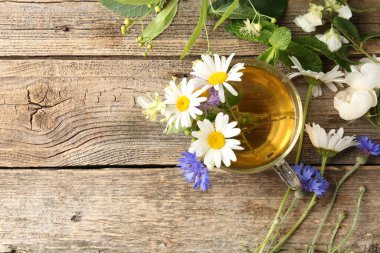 Cam bardakta Aromatik bitki çayı, tahta masada çiçekler ve yeşil yapraklar, düz yatak. Metin için boşluk