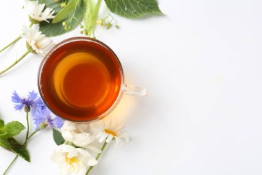Cam fincanda aromatik bitki çayı, farklı çiçekler ve beyaz arka planda nane şekeri, düz yatak. Metin için boşluk