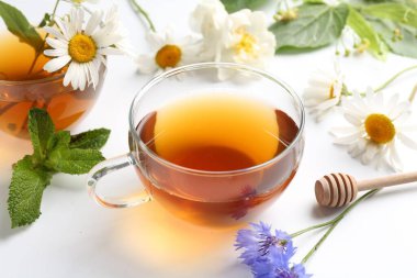 Cam fincanlarda aromatik bitki çayı, farklı çiçekler ve beyaz arkaplanda nane şekeri, yakın plan.