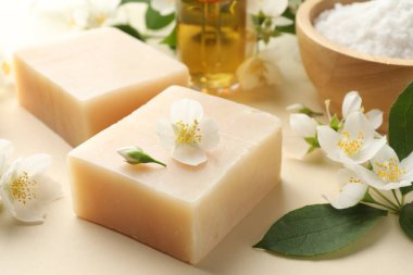 Sabun çubukları, temel yağ, deniz tuzu ve yasemin çiçekleri bej arka planda, yakın plan