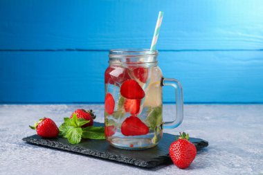 Çilekli içecek, limon ve naneli gri desenli masada mavi ahşap arka planda.