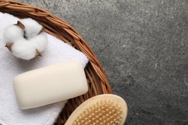 Sabun çubuğu, pamuk çiçeği, hasır sepetteki fırça ve havlu gri masada, üst manzara. Metin için boşluk