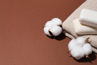 Sabun çubukları, pamuk çiçekleri ve kahverengi arka planda havlu, yakın plan. Metin için boşluk