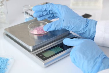 Bilim adamı beyaz masadaki terazide numune tartıyor, yakın plan.