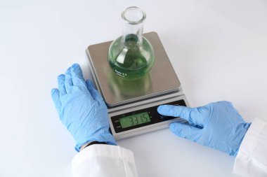 Bilim adamı beyaz masadaki terazide numune tartıyor, yakın plan.