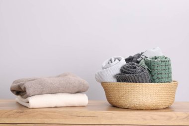 Katlanmış yün kazaklar ve atkılar hasır sepetin içinde, ahşap masanın üzerinde.