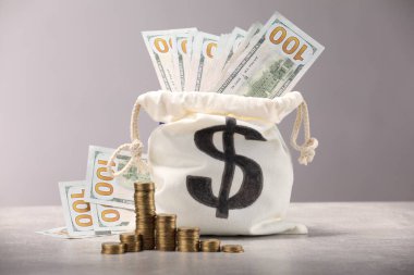 Dolar banknotlarıyla dolu çanta ve arka planda hafif desenli gri masalara istiflenmiş paralar.