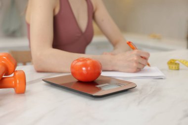 Beyaz mermer masada beslenme planı geliştiren kadın, mutfak ölçeğine ve domatese odaklan.