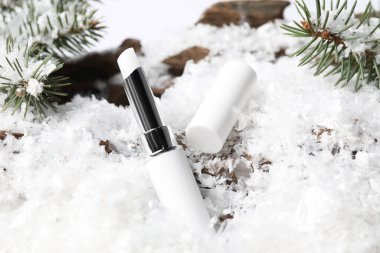 Nemlendirici dudak kremi ve suni kar üzerinde köknar ağacı dalları, yakın plan. Kış bakımı
