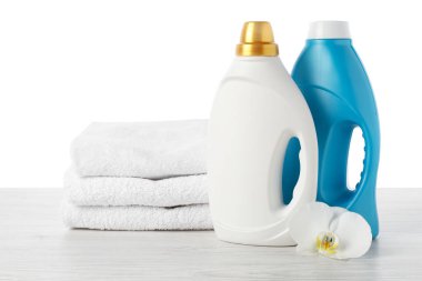 Kumaş yumuşatıcı şişeler, beyaz arka plana karşı ahşap masa üzerine istiflenmiş havlular ve çiçekler.