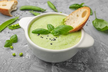 Lezzetli bezelye kremalı çorba fesleğen ve kızarmış ekmek, yakın plan, gri masada servis edilir.