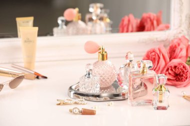 Farklı parfüm şişeleri, aksesuarlar ve çiçekler kapalı salonda.