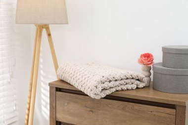 Yünlü battaniye, kutular, vazodaki güzel çiçek çekmecelerden yapılmış ahşap sandıkta ve beyaz duvarın yanındaki lamba, yakın plan.